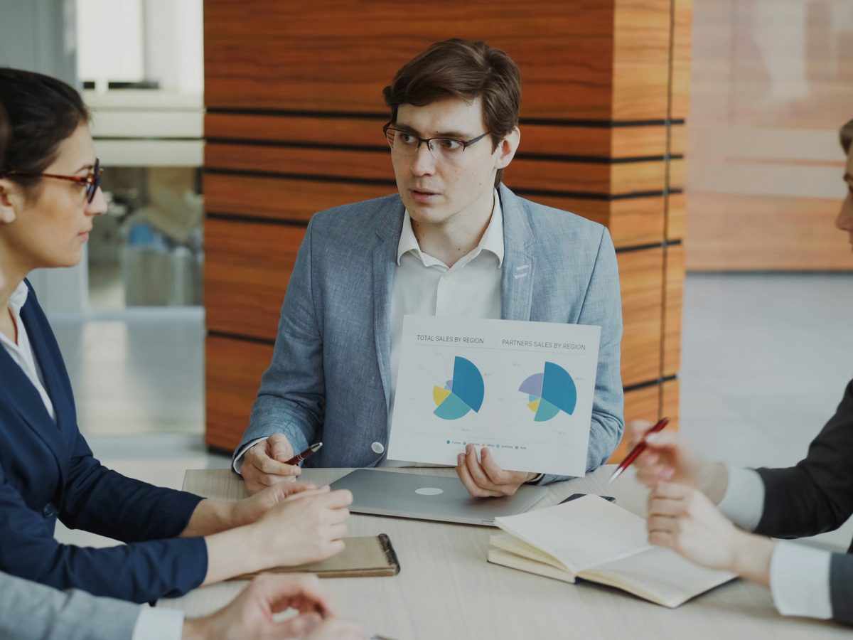A consultant talking through a sales-by-region chart with four colleagues around a conference table.